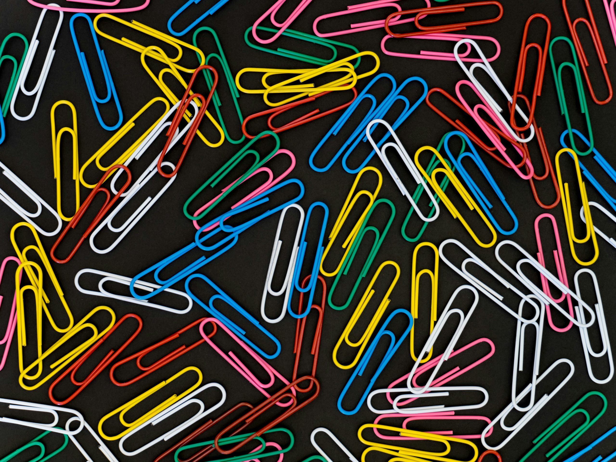 Many colorful paperclips on a dark grey background